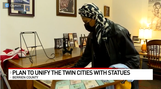 Sharon Brown in the art gallery - the news ticker reads "Plan to unify the Twin Cities with statues."