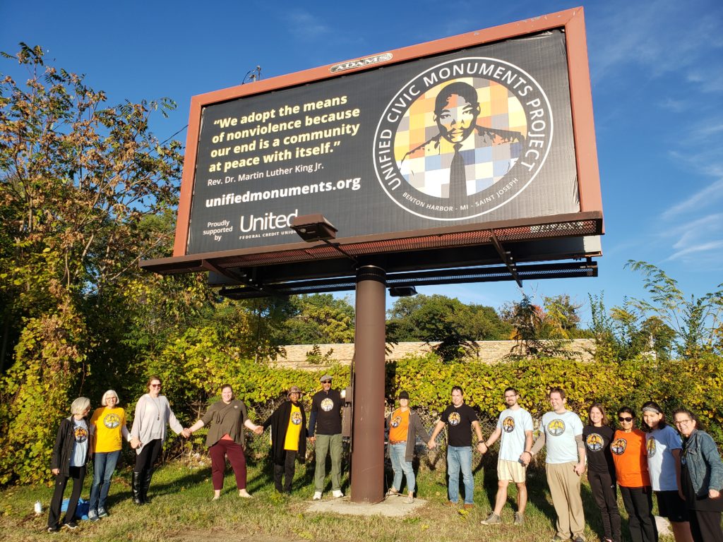 UCMP team holding hands under a UCMP billboard in Benton Harbor.